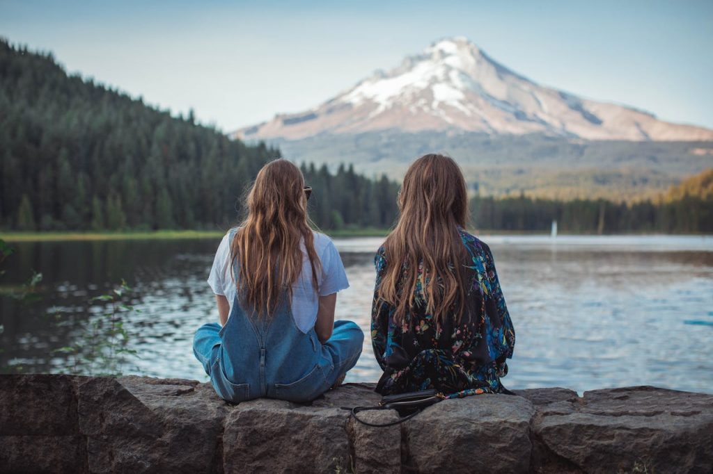 Two women sitting by a lake with a stunning view of Mount Hood in Oregon during sunset.